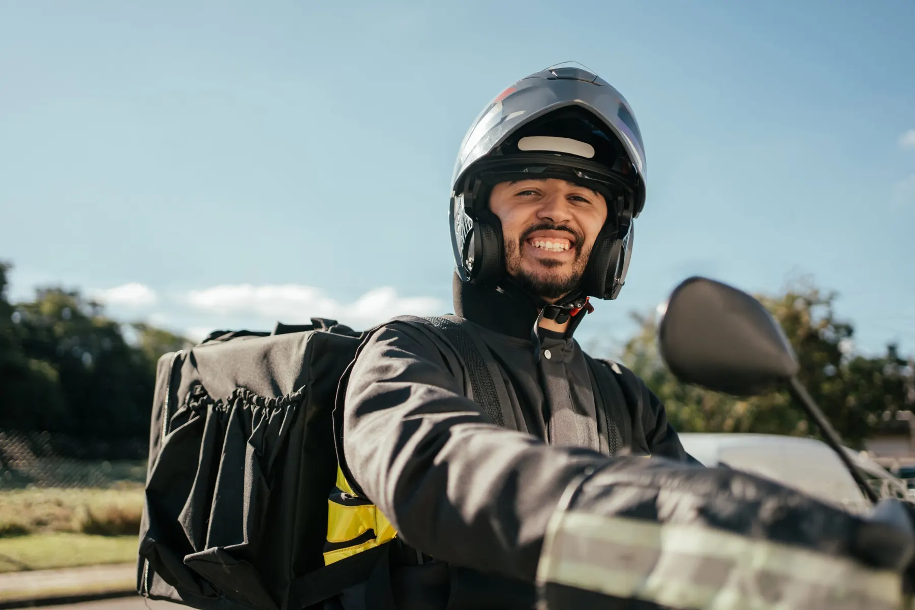 Entregador sorrindo de capacete, sentado na moto com a bag nas costas